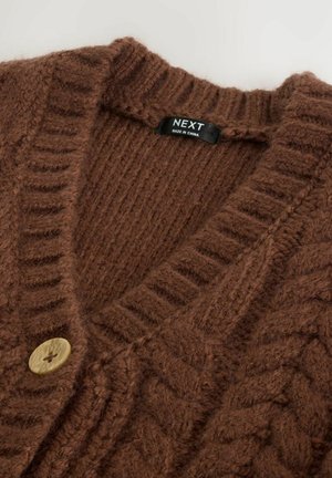 Brūna adīta kardigāna ar V-veida kaklu, ribotiem malām un struktūrētu kabeli. Satur koka pogu un zīmola etiķeti iekšpusē.