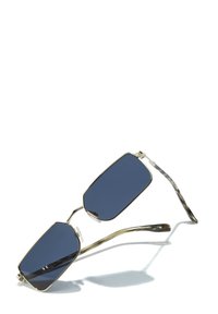 Lunettes de soleil avec des verres sombres octogonaux, monture en métal doré mince et branches à motifs. Plaquettes de nez réglables pour le confort.