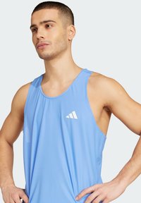 Svijetloplavi atletski tank top od prozračnog mrežastog materijala. Ima okrugli izrez i bijeli trokutasti logotip na prsima.