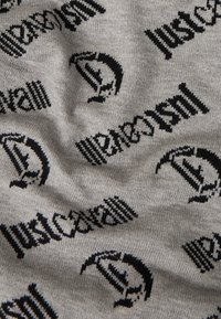 Țesătura gri are un model repetitiv cu logo-uri negre. Textura pare moale și tricotată, cu variații în design și detalii.