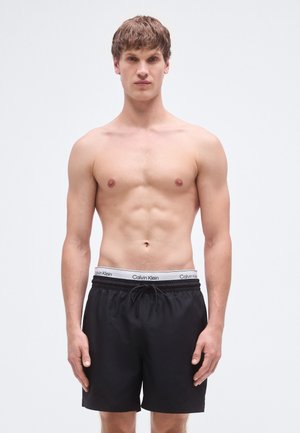 Bañador negro con cintura elástica que presenta un logo blanco de Calvin Klein, material ligero y un ajuste estándar.