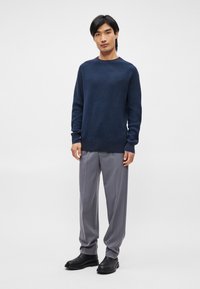 Pulover texturat albastru marin cu guler rotund, asortat cu pantaloni gri deschis, croiți, și cizme negre până la gleznă. O ținută simplă, modernă.