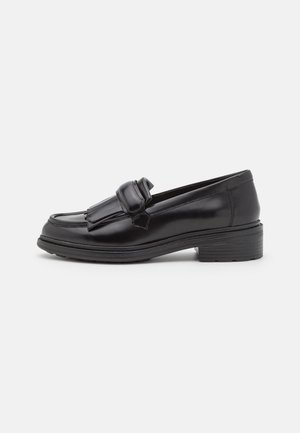 Mocassins en cuir noir avec un bout arrondi, détail de frange à l'avant et semelle en caoutchouc épaisse, présentant une texture lisse et un design minimal.