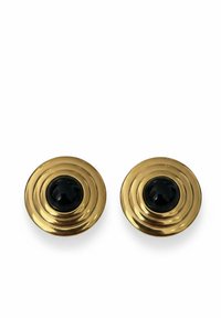 Gold circular earrings with concentric ridges and a central black bead. Smooth metal finish, reflecting light, creating a textured appearance.