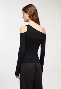 Czarny prążkowany top dzianinowy z jednym odsłoniętym ramieniem. Dopasowany fason z długimi rękawami i lekko rozszerzanym dołem. Gładka tekstura całości.