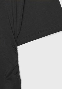 Gros plan d’un t-shirt noir à manches courtes montrant la texture du tissu, un détail froncé sur le côté et des coutures le long de l’ourlet de la manche.