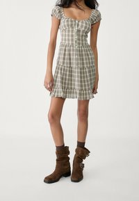 Krótka sukienka w kratę z bufkami, kwadratowym dekoltem, guzikami z przodu i warstwowym dołem. Połączona z brązowymi zamszowymi kozakiem.