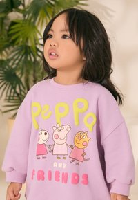 Vijolična jopa z ohlapnim krojem. Ponaša se z barvitimi risanimi liki in napisom »Peppa and Friends« z velikimi, kontrastnimi črkami.