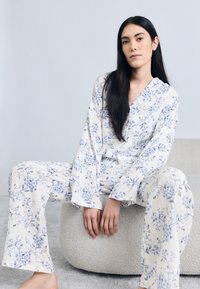 Ensemble de pyjama à imprimé floral crème avec des fleurs bleues ; chemise à manches longues avec col et tissu doux et texturé ; pantalon ample.