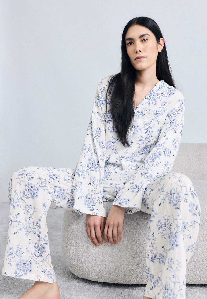 Ensemble de pyjama à imprimé floral crème avec des fleurs bleues ; chemise à manches longues avec col et tissu doux et texturé ; pantalon ample.