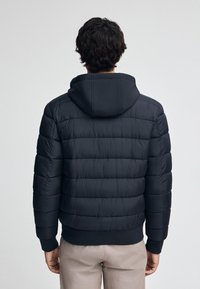 Czarna kurtka puchowa z poziomym pikowaniem, z kapturem i prążkowanym dołem. Tkanina wydaje się gładka i lekko błyszcząca.