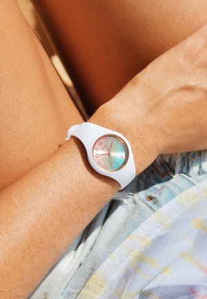 Weißer Silikonarmband mit einem runden Ziffernblatt, das ein mehrfarbiges, schimmerndes Ziffernblatt und silberne Stundenmarkierungen aufweist. Wird an einem Arm gegen Denim getragen.