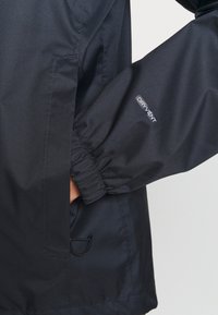 Nahaufnahme einer Hand in der Tasche einer schwarzen DryVent-Jacke mit elastischem Ärmelbündchen und verstellbarem Saumkordel.