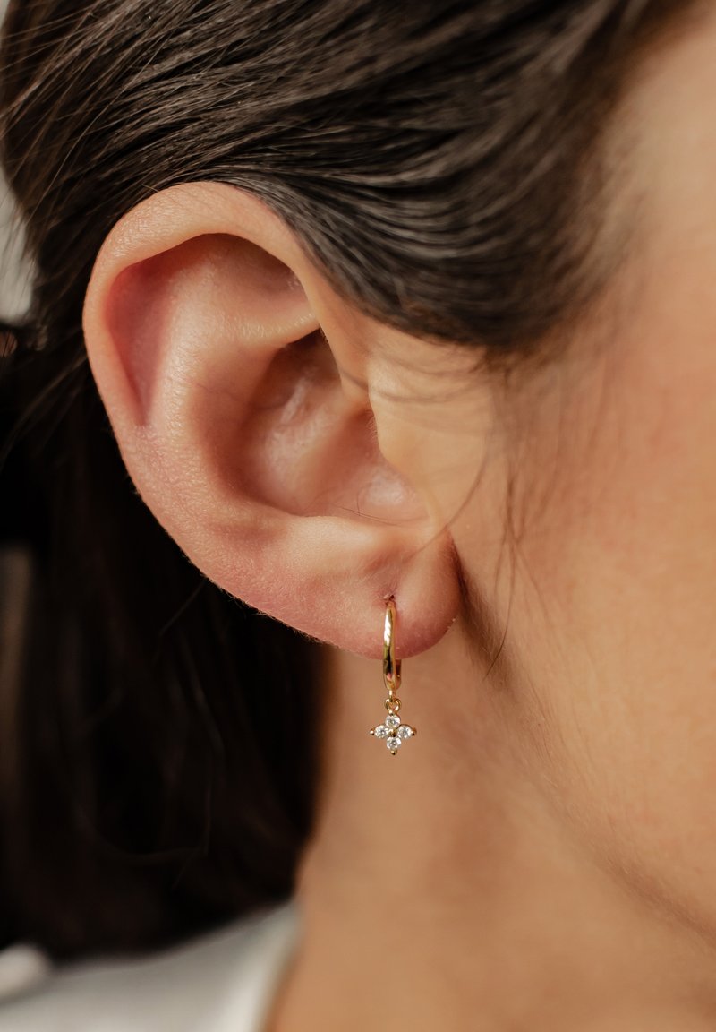 Pendiente de aro dorado con un pequeño diseño en forma de estrella, que presenta tres piedras preciosas transparentes. El pendiente cuelga justo por debajo del lóbulo de la oreja.