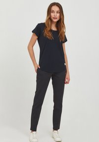 Mornarsko modra majica s kratkimi rokavi in okroglim ovratnikom, v kombinaciji s slim-fit črnimi hlačami in belimi superge. Preprost dizajn brez vzorcev.
