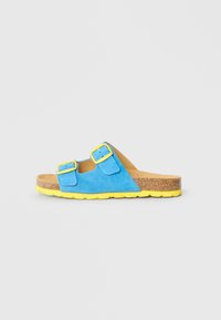 Μπλε σουέντ πέδιλο slide με κίτρινες αγκράφες, πάτο από φελλό και κίτρινη υφασμάτινη σόλα σε απλό ανοιχτό φόντο.