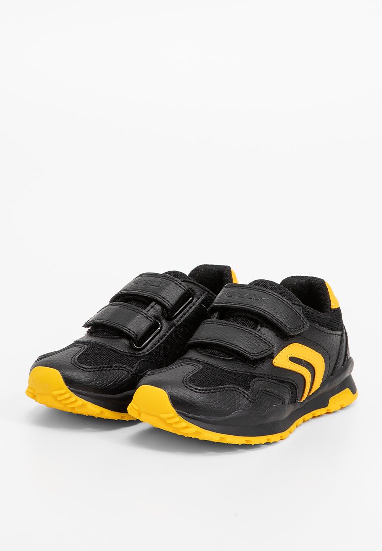 Baskets noires de sport avec des accents jaunes ; présentent une finition texturée et deux bandes velcro ajustables ; semelles rembourrées pour le confort.