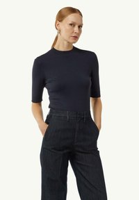 Granatowa bluzka z krótkim rękawem o dopasowanym kroju z okrągłym dekoltem, zestawiona z ciemnoniebieskimi spodniami z wysokim stanem z denimu. Teksturowana tkanina z niewielką elastycznością.