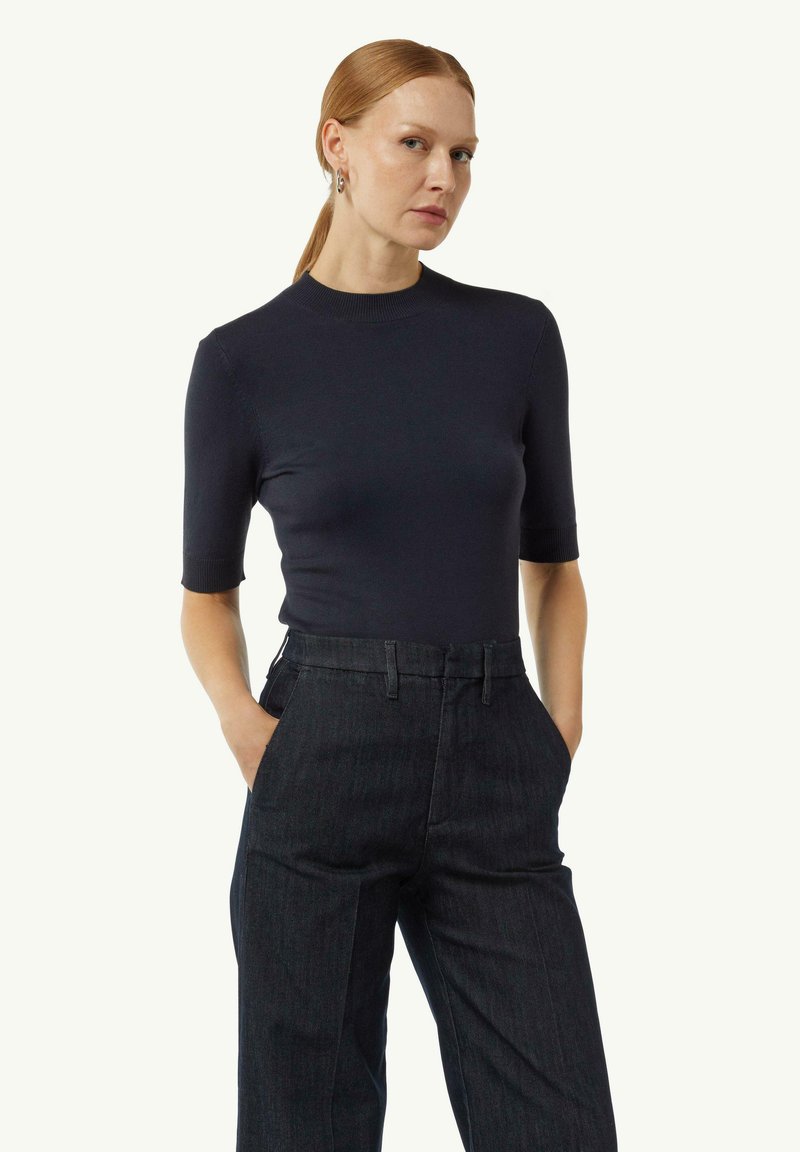 Granatowa bluzka z krótkim rękawem o dopasowanym kroju z okrągłym dekoltem, zestawiona z ciemnoniebieskimi spodniami z wysokim stanem z denimu. Teksturowana tkanina z niewielką elastycznością.