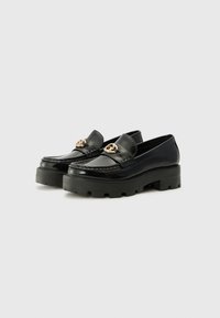 Zwarte lakleren loafers met een gouden embleem, voorzien van een dikke zwarte platformzool en decoratieve stiksels langs de randen.