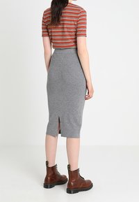 Šedá pletená tužková sukně s rozparkem na zadní straně, spárována s krátkým rukávem pruhovaným topem v červené a bílé barvě a hnědými šněrovacími kotníkovými botami.