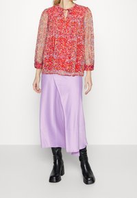 Blusa trasparente a maniche lunghe con motivo floreale rosso e scollatura a oblò; abbinata a una gonna liscia, lavanda, di lunghezza intermedia e stivaletti neri alla caviglia.