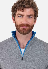 Pull gris avec un col zippé bleu. Le tissu semble tricoté, avec une fermeture à demi-glissière et des coutures contrastantes le long de la fermeture éclair.