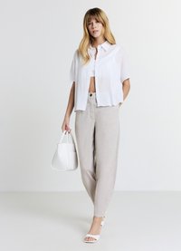 Chemise blanche courte à boutons, pantalon en lin beige clair, sandales blanches à talon bloc, et un petit sac à main blanc, avec une texture lisse.