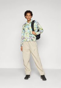 Večbarvna lahka jakna z abstraktnimi cvetličnimi vzorci, združena z bež hlačami s številnimi žepi in črnimi pohodniškimi čevlji. Vključen je tudi črn nahrbtnik.