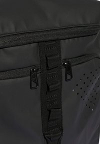 Mustasaari, joka on valmistettu kestävästä materiaalista. Varustettu vetoketjukiinnityksellä, verkkostringeillä ja ilmanvaihtorei'illä yhdellä sivulla hengittävyyden takaamiseksi.