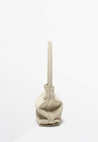 Beige suede handbag shown from the side with a single narrow handle and soft, slouchy structure against a plain white background.