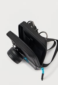 Saco de câmera preto feito de tecido texturizado, com um compartimento com fecho, correia ajustável e destaque azul na puxador do fecho.