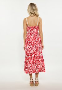 Vestido rojo con estampados florales blancos, corpiño ajustado y tirantes finos ajustables, que fluye en una falda en capas. Espadrilles de yute natural.