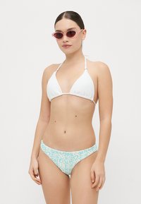 Biely trojuholníkový bikiny top s textúrovanou textíliou, spárovaný s svetlomodrými a bielymi spodnými bikiny s kvetinovými vzormi. Rúžové slnečné okuliare.