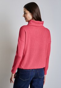Pullover aus weichem Korallenstoff mit einem hohen Kragen, lockerer Passform und langen Ärmeln; kombiniert mit dunkelblauen Jeans; minimalistisches Design.