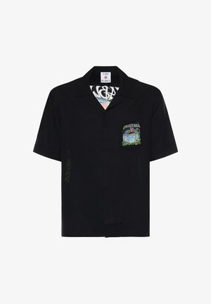Chemise noire à manches courtes avec col, poche avant ornée d'une scène de plage avec palmiers, océan et coucher de soleil, étiquetée « Casa Blanca ».