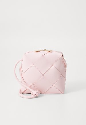 Bolso bandolera de cuero tejido en rosa suave con cremallera dorada y correa ajustable anudada en la base, sobre un fondo blanco.