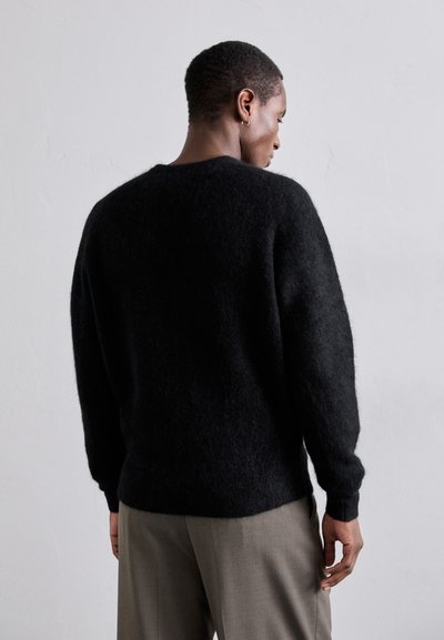 Suéter negro de lana esponjosa con un corte holgado, que presenta mangas largas y un escote redondo, combinado con pantalones gris claro.