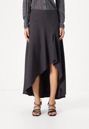 Lange, kolengrijze rok met een asymmetrische zoom en een gladde textuur. Gecombineerd met zwarte sandalen met hakken en bandjes.