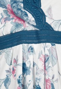 Robe à motifs floraux avec une base blanche, ornée de designs bleus et roses. Elle est dotée d'une bande d'accent texturée bleue avec des détails en dentelle.