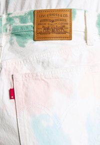 Jeans de mezclilla blanca con teñido anudado en tonos pastel verde y rosa, con una etiqueta de cuero marrón de Levi Strauss & Co. y una etiqueta de tela roja en el bolsillo trasero.
