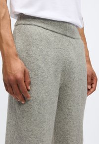 Ανοιχτό γκρι, μαλακά παντελόνια από μάλλινο ύφασμα με λεία υφή και ελαστική μέση, εμφανίζονται με ένα χέρι να ακουμπάει στο ύφασμα.