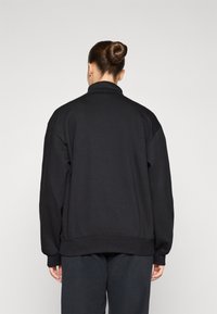 Felpa nera con vestibilità comoda, collo alto e spalle scese. Texture liscia con polsini e orlo a coste, design minimalista.