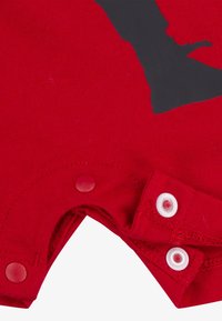 Un body en coton rouge avec un design graphique noir, doté de boutons-pression en bas et d'une texture lisse. Les bords sont cousus pour plus de durabilité.