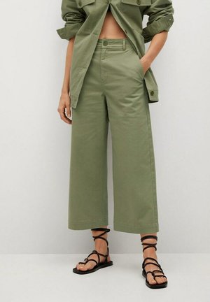 Pantalones de pierna ancha verde oliva hechos de algodón, con una cintura de altura media, bolsillos laterales y un acabado limpio. Combinados con sandalias negras de tiras.