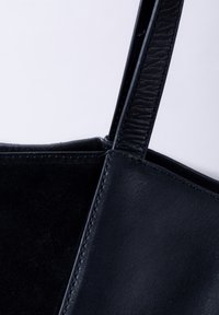 Black handbag featuring a combination of smooth leather and suede textures, with a structured shape and a flat, adjustable strap.