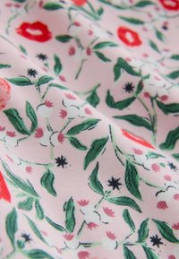 Floral fabric featuring a pink background with red and white flowers, green leaves, and small black accents. Soft texture and detailed pattern.