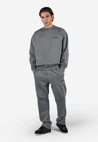 Grauer Sweatshirt und passende Hose aus weichem Material, mit lockerer Passform und minimalistischem Design, das den Markennamen in Schwarz zeigt.