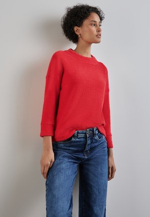 Maglione a maglia rossa con texture, scollatura ampia a girocollo, maniche a tre quarti, abbinato a jeans in denim blu a vita media.