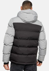 Chaqueta tipo puff con parte superior gris claro y parte inferior gris oscuro. Tiene capucha, secciones acolchadas y puños elásticos. Diseño sencillo y textura suave.